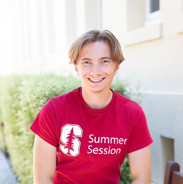 Adam wears a red Summer Session shirt and stands outside.